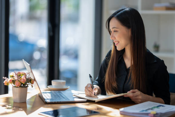 istock Attentive businesswoman jotting down notes while working on a project with her laptop at a sunny table. 2167777593