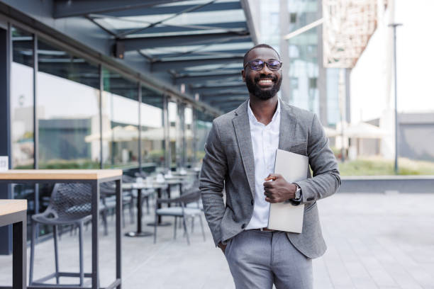 istock Confident businessman standing outside modern office building with laptop 2167779504