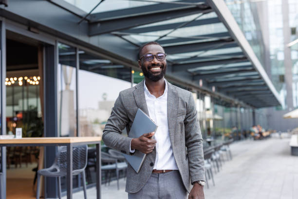 istock Confident businessman smiling outdoors holding a laptop in urban setting 2167779508
