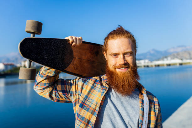 istock handsome redhaired man with long beard skateboarding near river at sunny summer day 2167780222