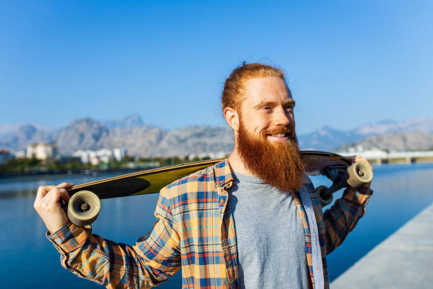 istock handsome redhaired man with long beard skateboarding near river at sunny summer day 2167780225