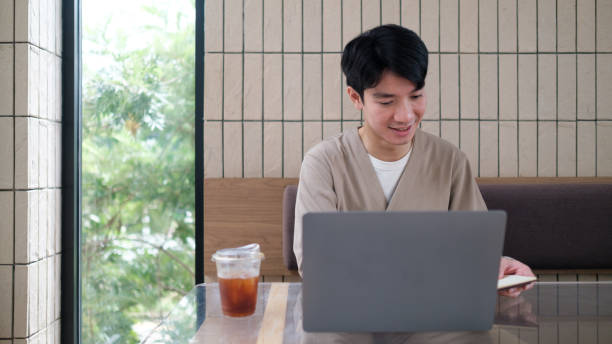 This image captures a young man working on his laptop in a modern, well-lit cafe.