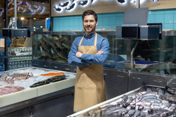 Confident fishmonger standing in front of seafood display at fish market