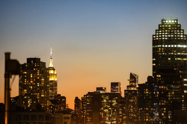 This is photograph of the NYC Skyline with the Empire State building and other skyscrapers illuminated at dusk.