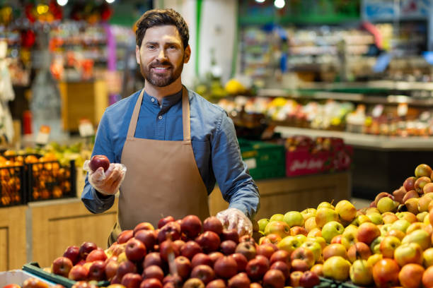 istock Smiling shopkeeper holding apple at fruit stand in grocery store 2167794343