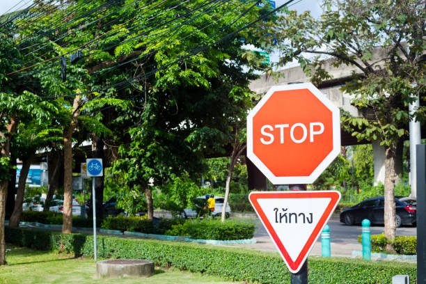 Stop sign and caution in thai language in front of trees at main road Pradit Manutham Rd in  Bangkok Lat Phrao for cars coming from driveway Crystal Park shopping center and luxury village park