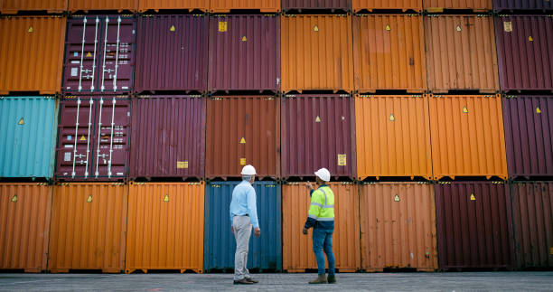 istock Business people, logistics and pointing with container yard in distribution or stock control at depot. Businessman, distributor or supplier in discussion for supply chain, shipment or drop at storage 2167803139