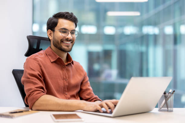 istock Smiling man working on laptop in modern office environment 2167805935
