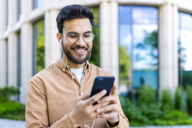 istock Smiling man using smartphone outdoors while listening to music with earphones 2167807990