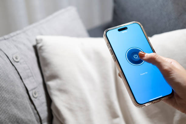 Smart home concept Controlling lights, lamps, or home appliances through a mobile application. A woman's hand is turn off the lights through her phone on the bed or sofa in the house