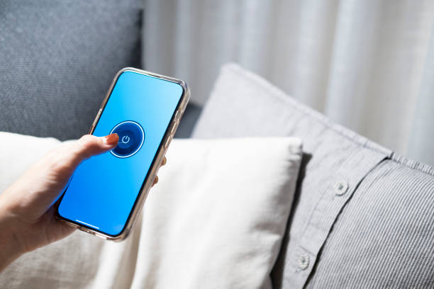 istock Smart home concept Controlling lights, lamps, or home appliances through a mobile application. A woman's hand is turn off the lights through her phone on the bed or sofa in the house 2167809603