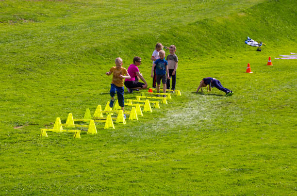 A small group of children raise their hands in the air as they cross the finish line first during a Cross Country race. They are each dressed comfortably in athletic wear and are smiling as they proudly cross the finish line.