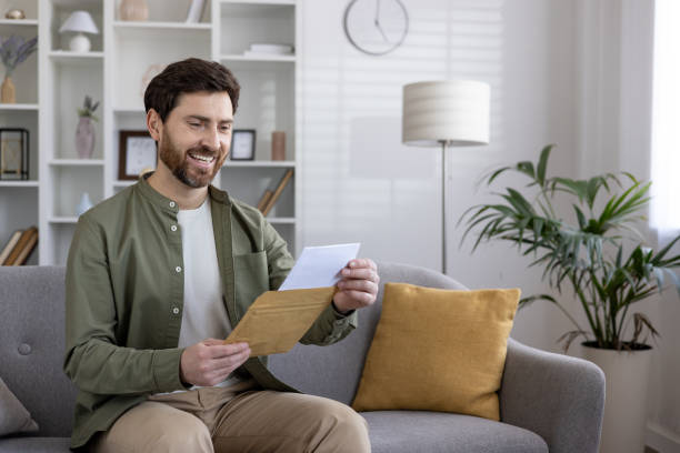 istock Smiling man reading letter on couch in modern living room 2167813256