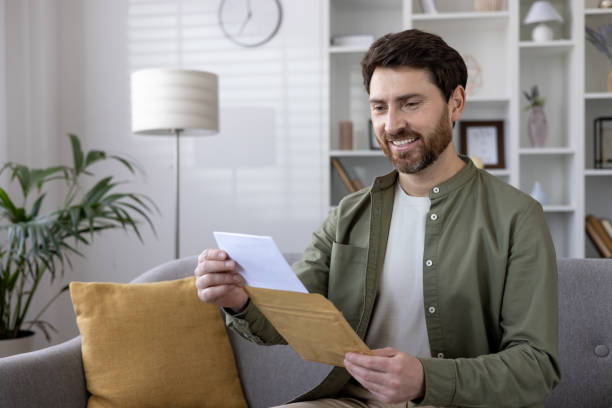 istock Smiling man opening a letter at home while sitting on the couch 2167813463