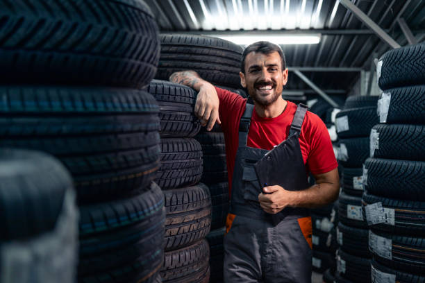 Working in tire warehouse. Portrait of smiling warehouse worker standing by the pile of new car tires. auto parts warehouse stock pictures, royalty-free photos & images