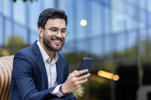 istock Hispanic businessman smiling while using smartphone outside modern office building 2167824872