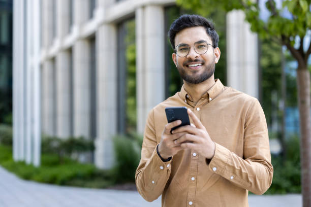 istock Smiling young man using smartphone outside modern office building, wearing casual outfit 2167825519