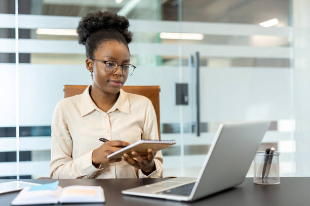 istock Businesswoman having a video call in modern office setting, taking notes on notepad, working on laptop 2167826072