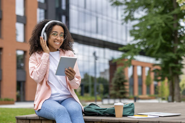istock Young woman using digital tablet with headphones outdoors on campus 2167826354