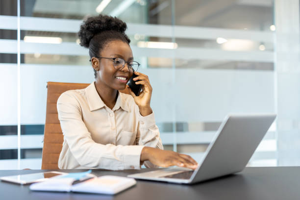 istock Smiling businesswoman talking on phone while working on laptop in modern office 2167829269
