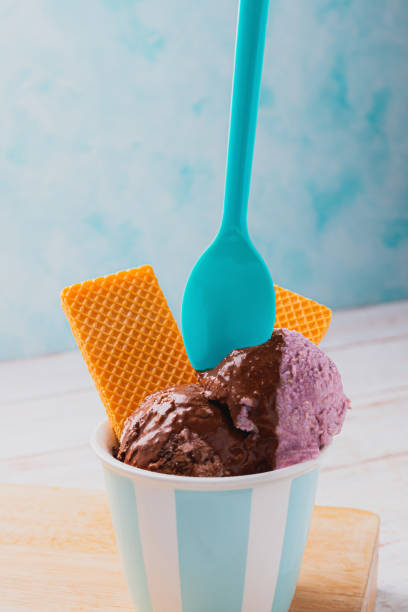 istock Colored plastic spoon stuck on ice cream scoop with chocolate sauce. waffer cookies. Bright turqoise background. 2167829792