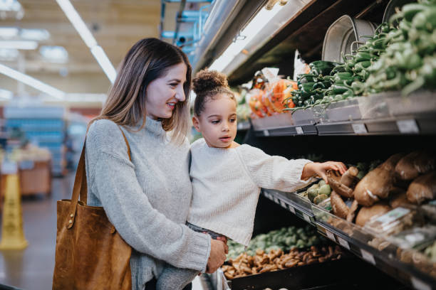 istock Mother holds her daughter while picking out vegetables at the store 2167830364