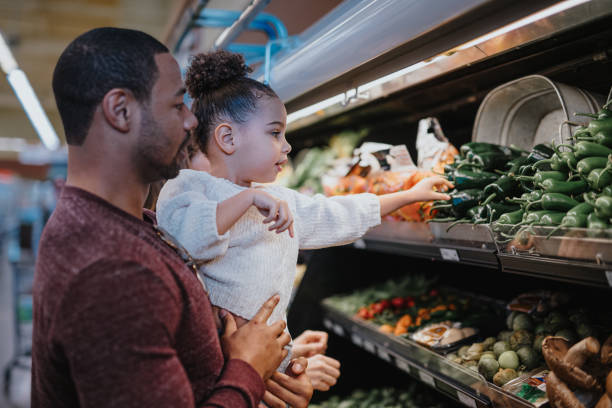 istock Father holds his daughter while picking out vegetables at the store 2167830367