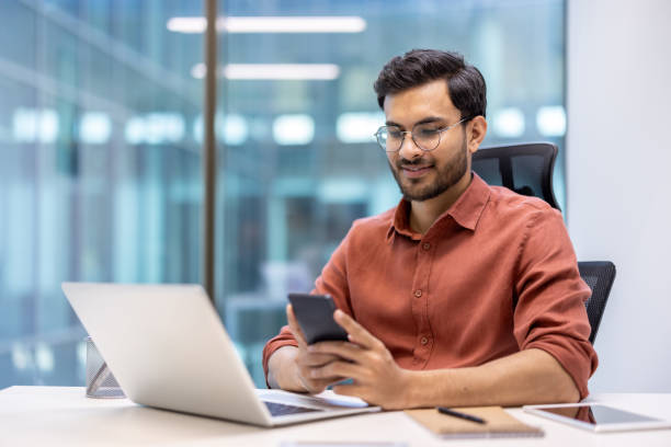istock Young professional working at desk in modern office using smartphone and laptop 2167832356