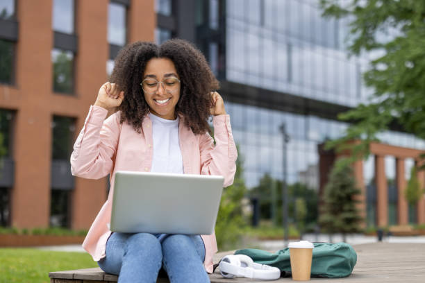 istock Woman celebrating success while working on laptop outdoors at modern campus 2167834301
