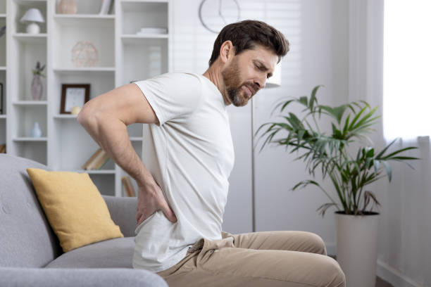 istock Man experiencing back pain while sitting on couch at home, suffering from discomfort or injury 2167835848