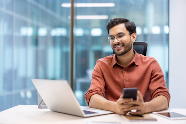 istock Smiling professional working on laptop and using smartphone in modern office 2167835964
