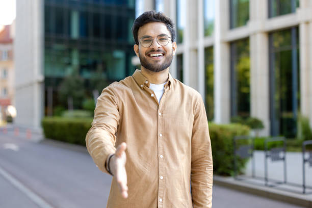 Smiling man extending hand for handshake outside modern building