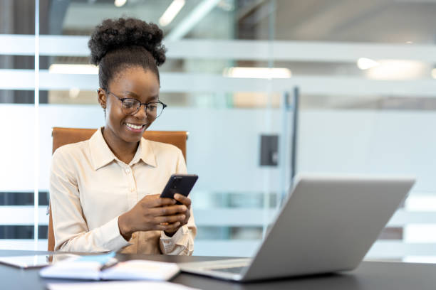 istock Smiling woman using smartphone at office desk with laptop 2167837313