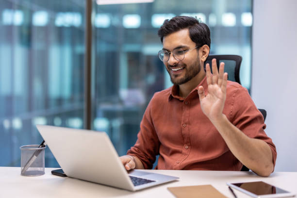 istock Happy businessman waving during a video call on laptop in modern office setting 2167837456