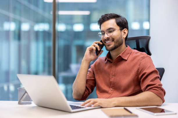 istock Smiling businessman talking on smartphone while working on laptop in office 2167837545