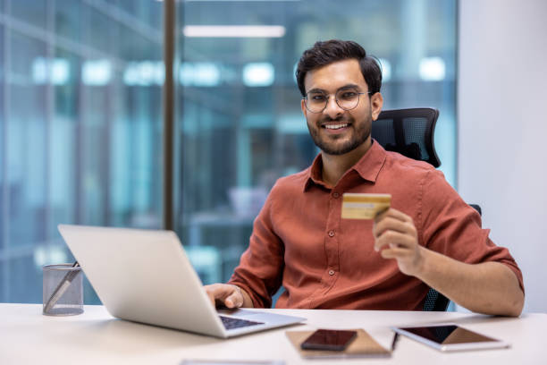 istock Smiling man holding credit card and using laptop in modern office environment 2167839749