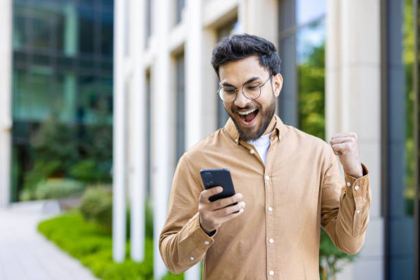 istock Excited man triumphantly looking at smartphone outdoors celebrating success 2167839883