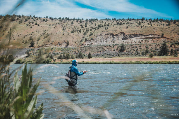 istock Fisherman stands waist deep in the river while casting his fishing pole 2167840695