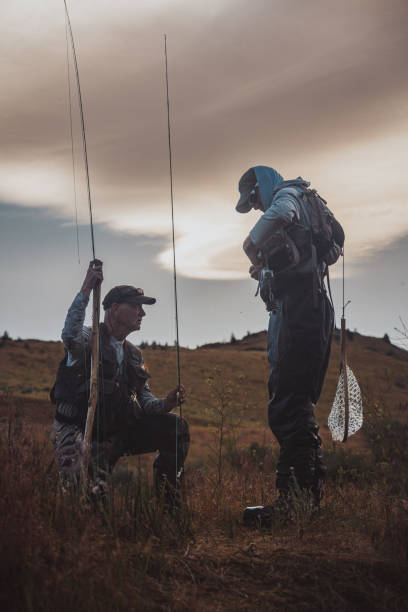 istock Fisherman kneels on the ground while chatting with his friend 2167840764