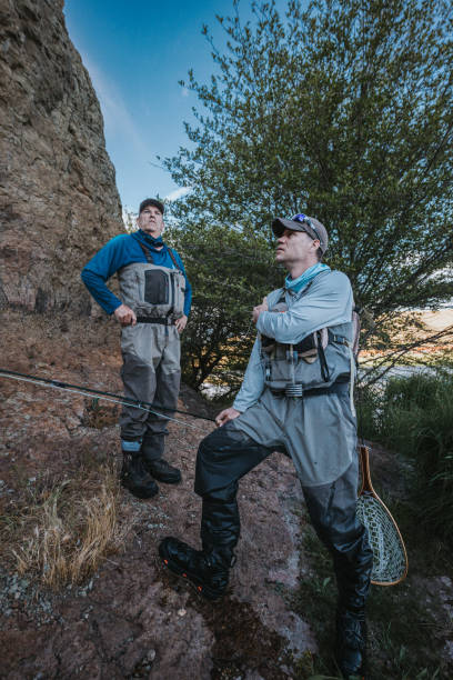 istock Two fishermen stand on high rocks beside the river 2167840873