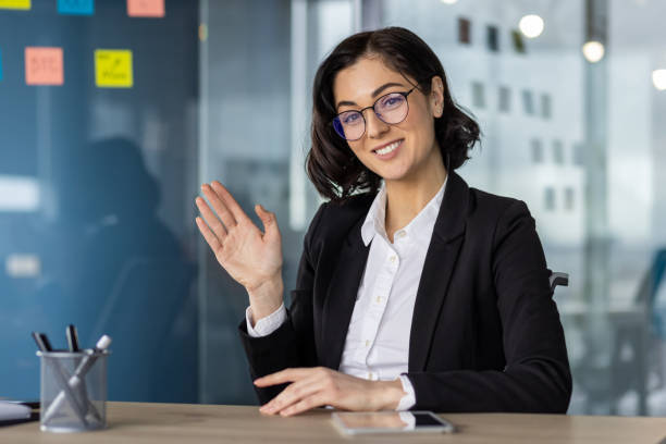 istock Businesswoman waving during video call in modern office setting 2167841516
