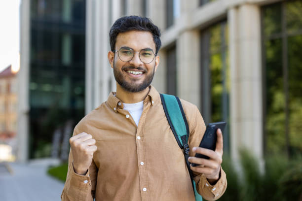istock Happy hispanic student celebrating success with phone outside campus building 2167841997