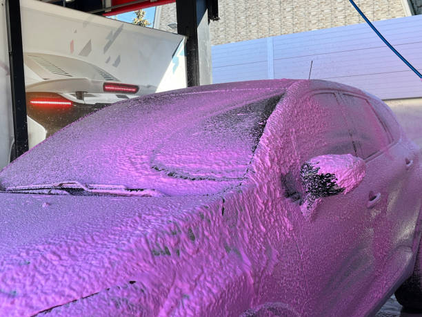 vehicle front bumper with parking sensor covered with a layer of active white foam with pink wax, car wash and car body care.