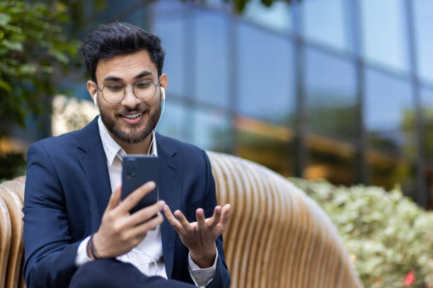 istock Young professional having video call outdoors, smiling man in business attire using smartphone and earbuds 2167844489