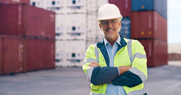 istock Portrait, happy man and confident mature engineer at container yard for export industry. Face, arms crossed and logistics manager at docks with safety helmet or glasses outdoor for import or shipping 2167844617