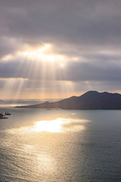 istock Sunbeams Through Clouds Over Serene Coastal Waters and Distant Islands 2167844650