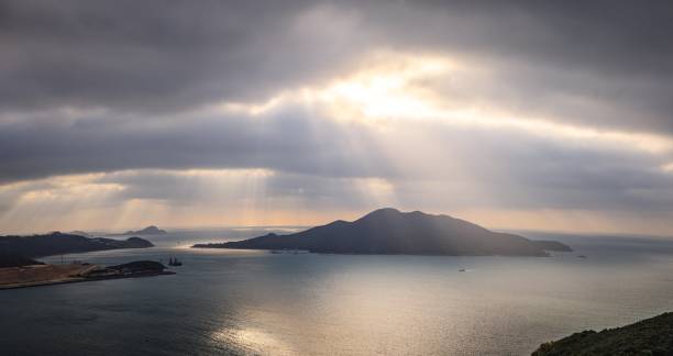 Sunbeams Through Clouds Over Serene Coastal Waters and Distant Islands