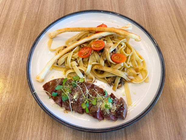A plate of grilled steak served with fettuccine pasta, cherry tomatoes, and breadsticks.