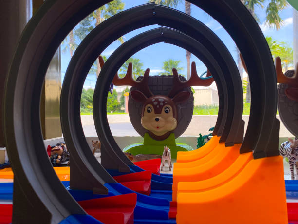 A close-up view of a toy race track with colorful curves and animal figures, with a window view of palm trees in the background.