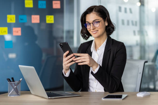 istock Businesswoman using smartphone in modern office with laptop and sticky notes 2167845853